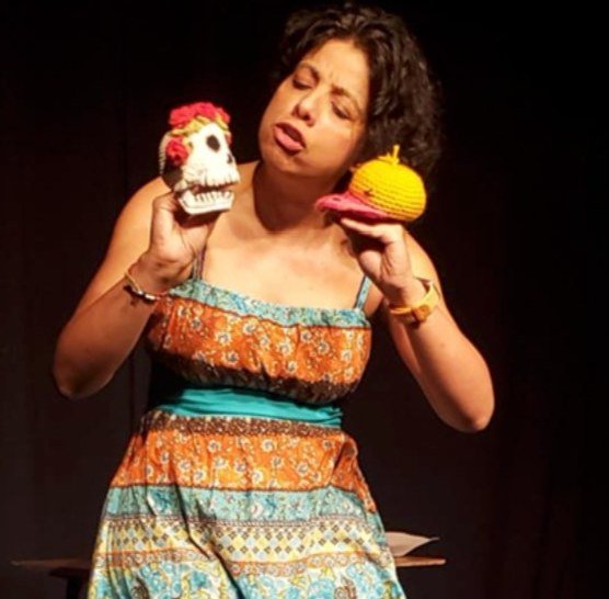 Karla Sepúlveda en escena, sosteniendo dos títeres tejidos